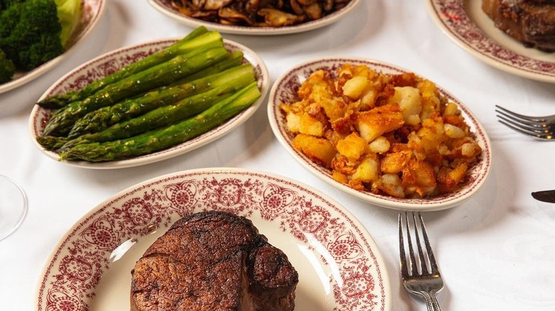 Bowls of crispy roasted potato hash browns and asparagus next to steak on plate