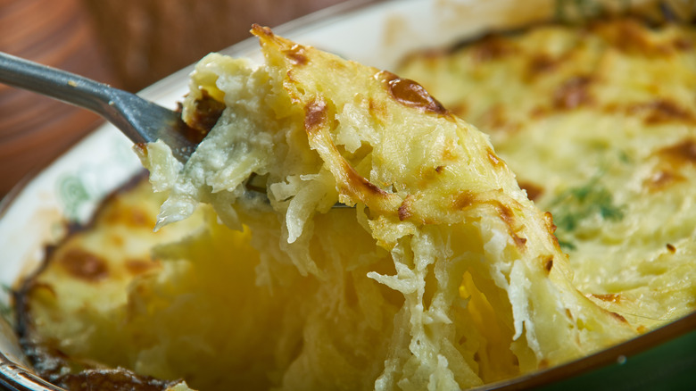 Spooning cheesy potatoes Romanoff from baking dish