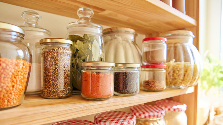 glass jars of various spices and other foods on light wooden shelves in bright light