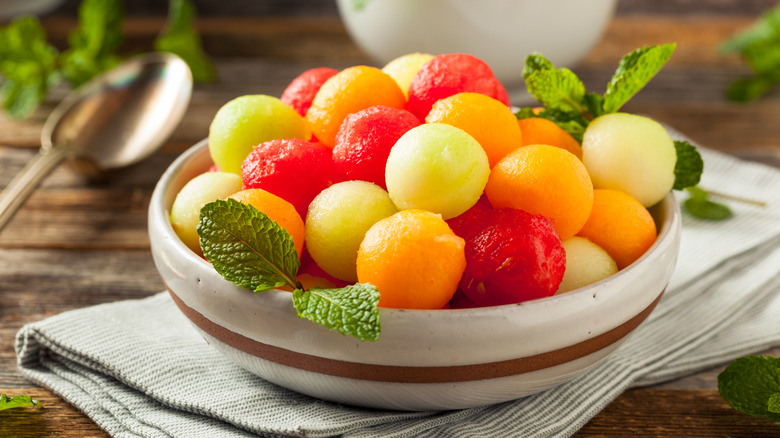 Balls of watermelon, honey dew, and cantaloupe in a bowl with mint sprigs