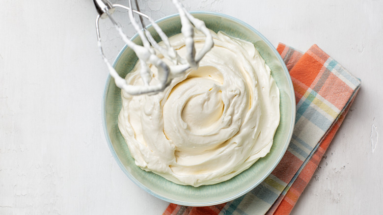 A small bowl of whipped cream with mixer whisks resting on the edge