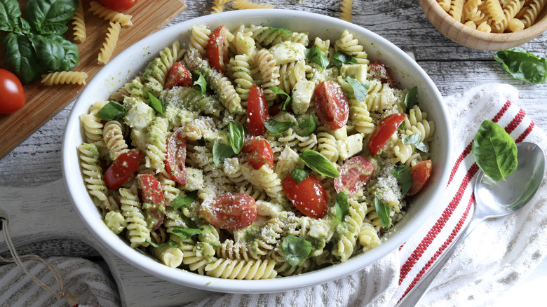 A large white bowl of rotini pasta salad with cherry tomatoes, basil, and cheese