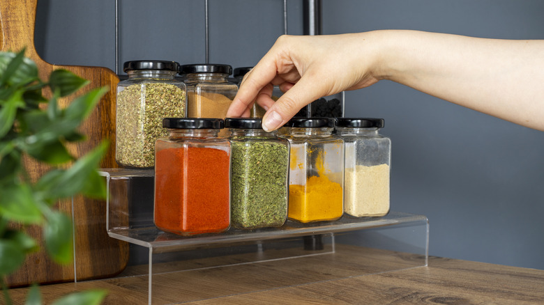 A person's hand reaching for jars of spices on a kitchen counter