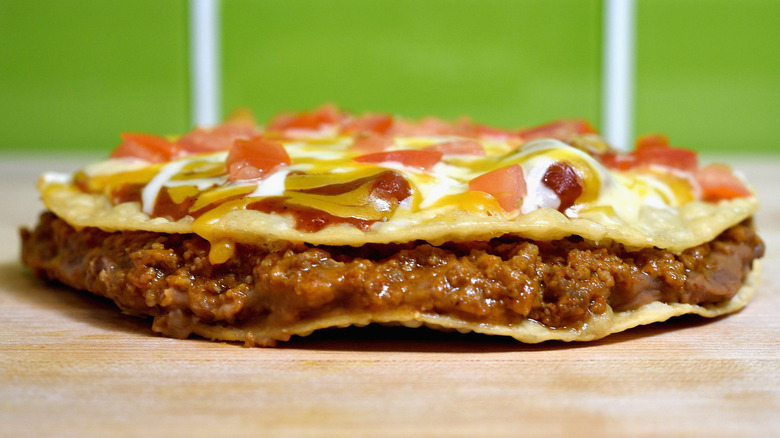 A Taco Bell Mexican Pizza on a wooden countertop with green tiles in the background
