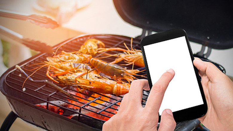 Overhead view of person standing over grill with phone