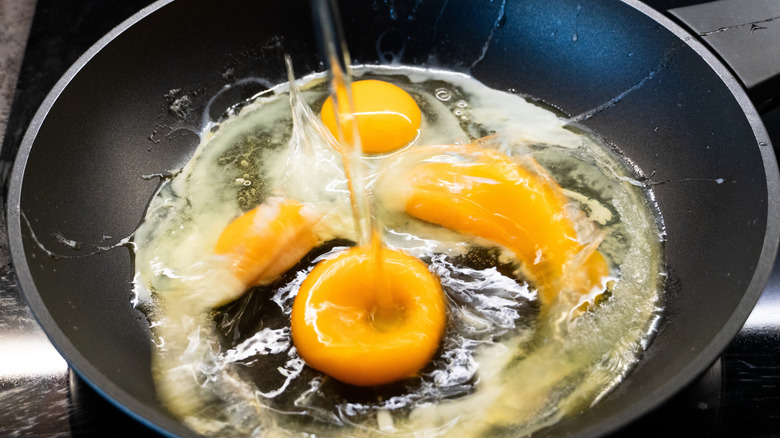 A raw egg splashing violently into a pan full of other eggs