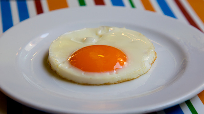 A perfect fried egg sitting on a white plate against a colorful background