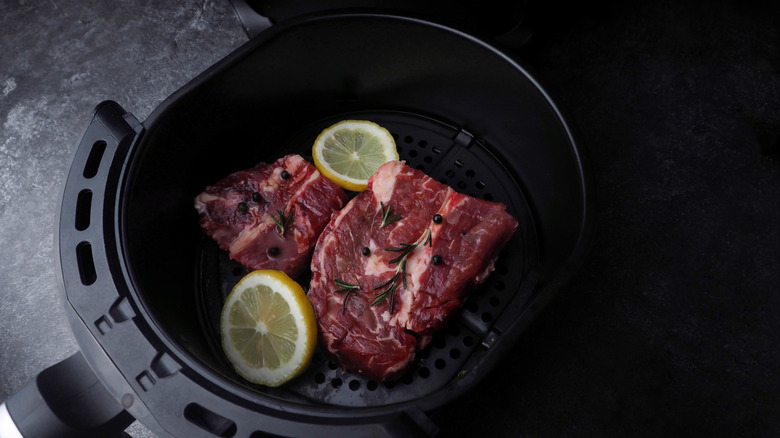 Raw steak with lemon slices and herbs in an air fryer basket