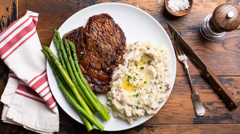 A plate of steak, mashed potatoes, and asparagus on a wooden table