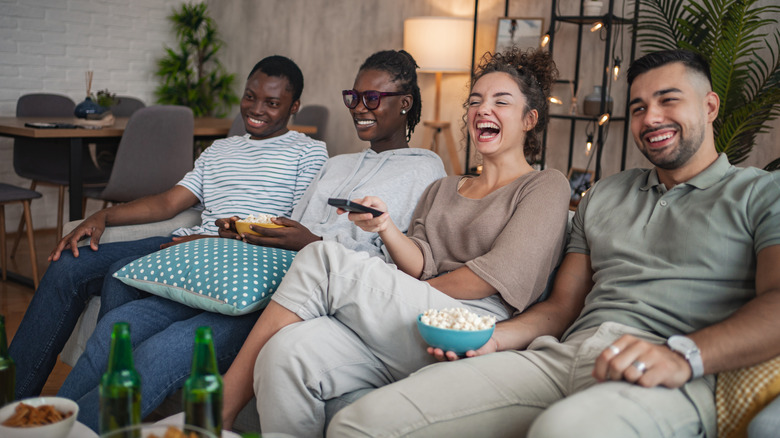 group of four young adults watching TV from a couch