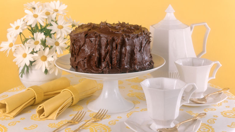 frosted chocolate cake on a white cake stand with tea setup