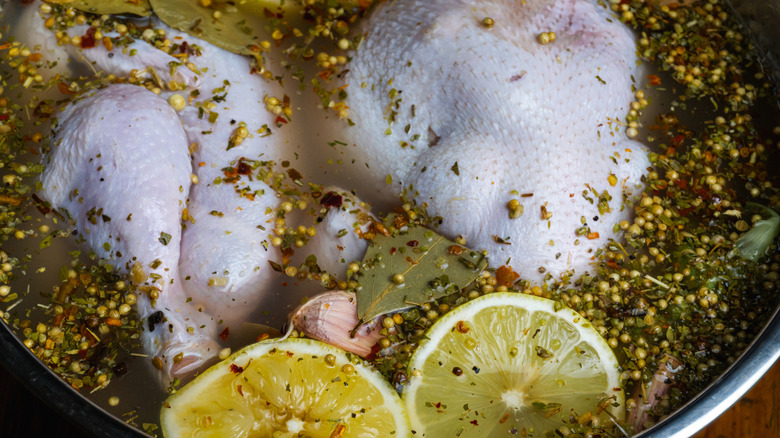 Chickens brining in a large stock pot with herbs, spices, and lemon, seen from above