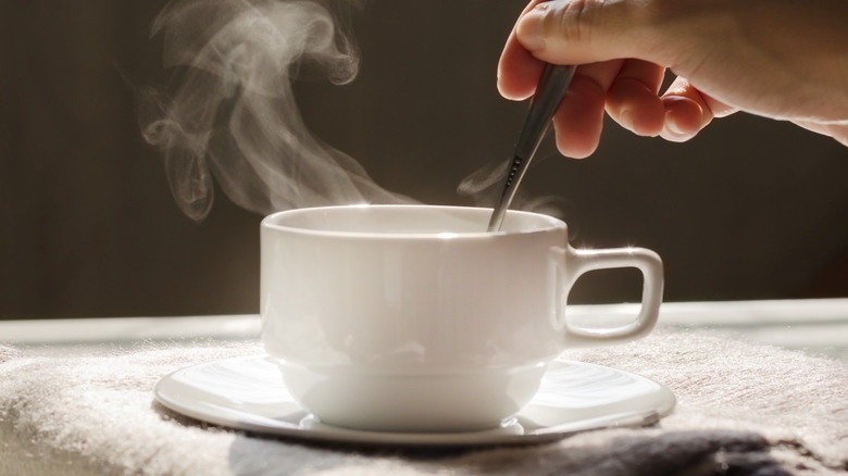 Hand stirring steaming liquid in a mug