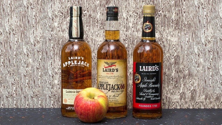 Three bottles of Laird's Applejack against woodgrain with an apple.