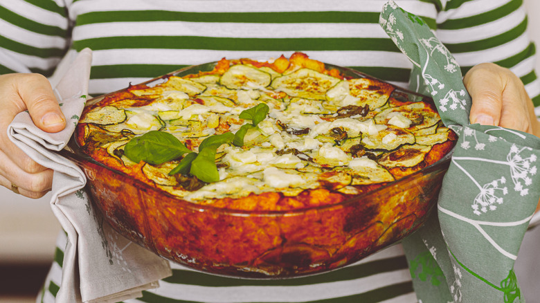 Hands holding large zucchini casserole with tea towels