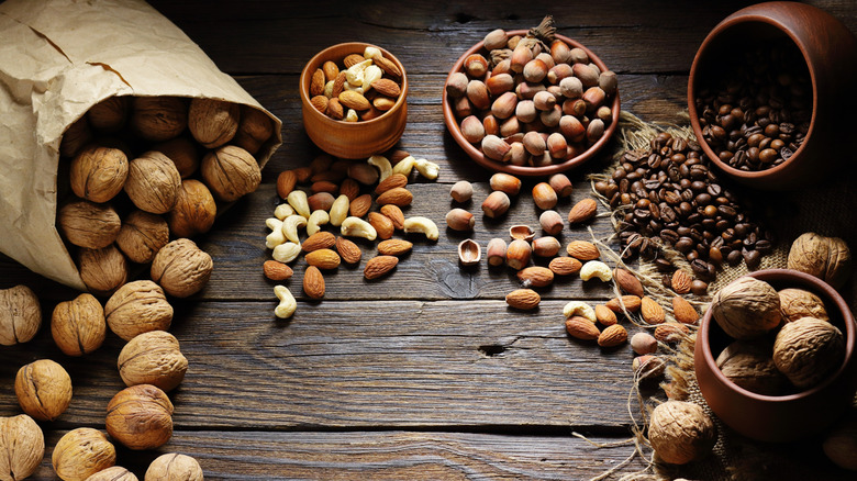 A variety of nuts including walnuts, almonds, and cashews with some coffee beans on a wooden table