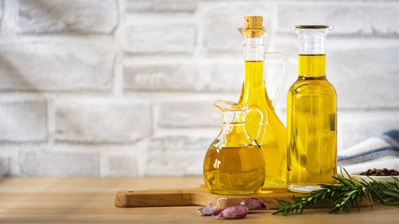 Three bottles of olive oil on the counter along with garlic and rosemary
