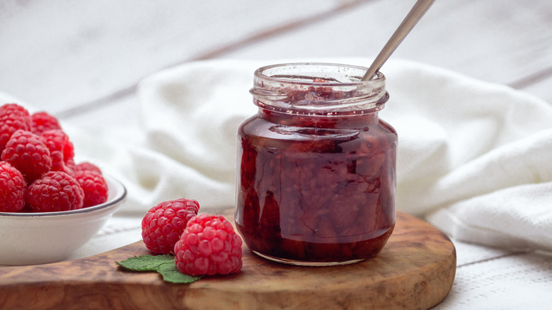 An open jar of raspberry jam with fresh rasberries on the side