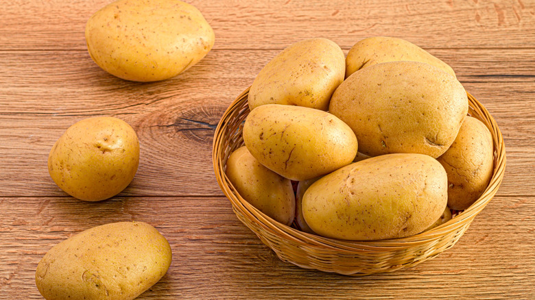 Potatoes in a basket and around it on a wooden surface
