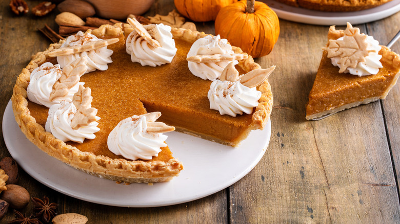 A whole pumpkin pie with a slice taken out