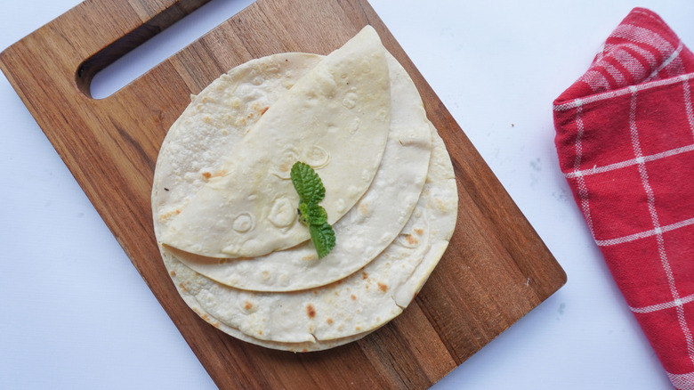 A wooden cutting board with a few tortillas on it
