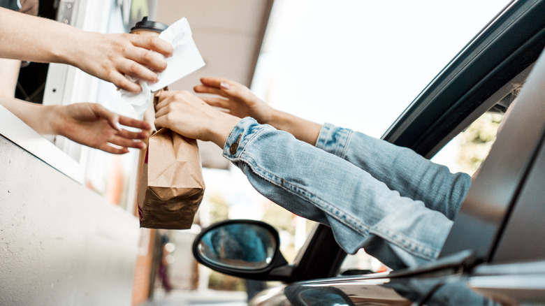 A bag of food and a coffee are handed from a drive-through window into a car