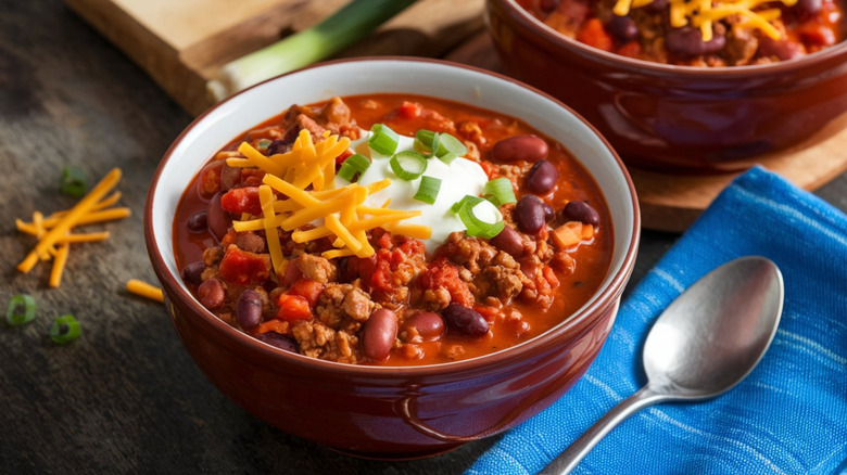 A bowl of meat and bean chili topped with sour cream, shredded cheese, and scallions