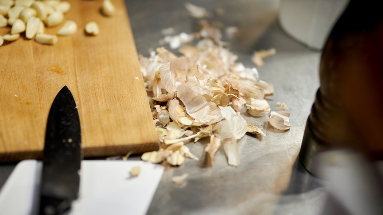 a pile of garlic skins next to a knife and a chopped board with garlic cloves