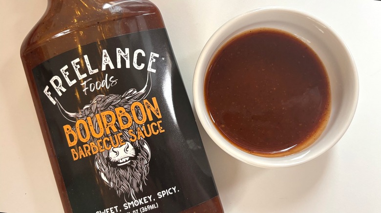 Bottle of Freelance Bourbon Barbecue Sauce next to small white bowl of sauce on white table