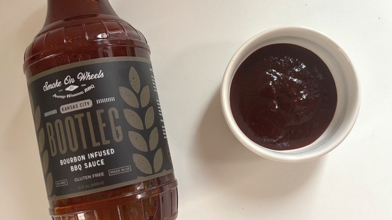 Bottle of Smoke on Wheels Bootleg Bourbon BBQ Sauce next to small white bowl of sauce on white table