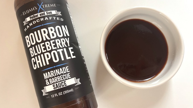 Bottle of Elijah's Xtreme Bourbon Blueberry Chipotle BBQ Sauce next to small white dish on white table