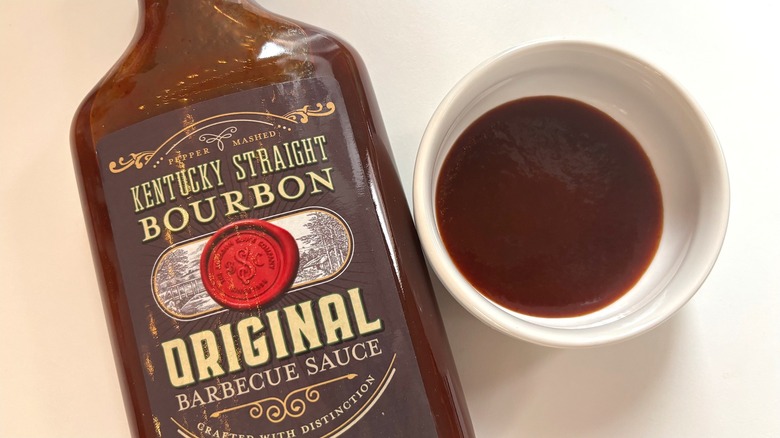 Bottle of Kentucky Straight Bourbon Barbecue Sauce next to small white dish of sauce on white table