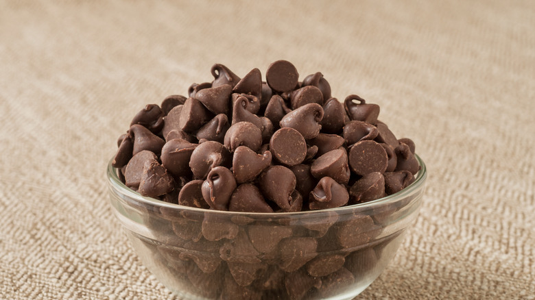 A glass bowl of chocolate chips on a textured tablecloth