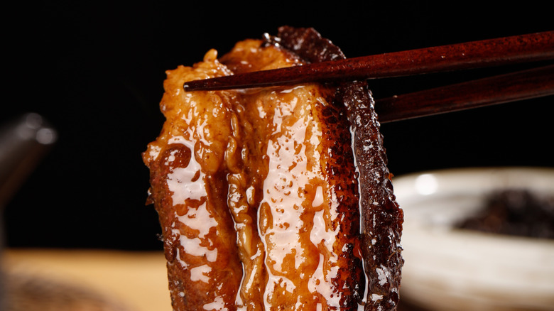 Chopsticks holding a piece of glazed pork belly