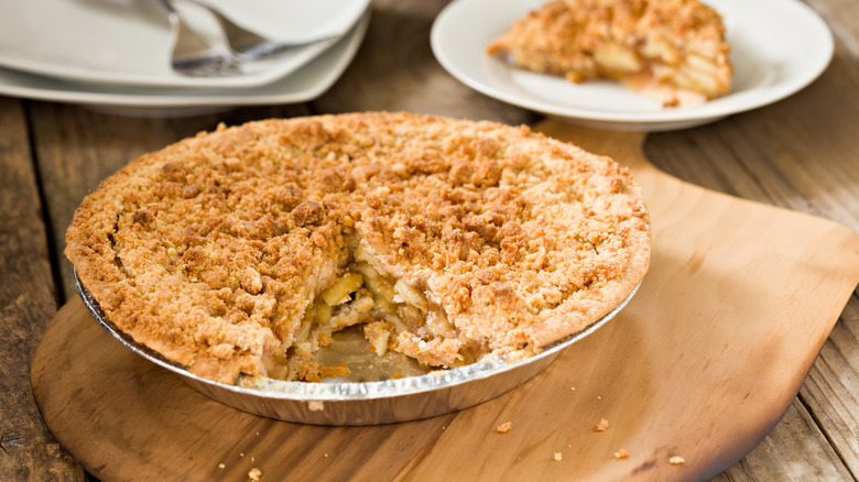 Dutch apple pie in a foil dish, with a slice served on a plate in the blurred background