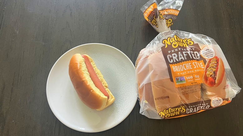 Nature's Own Brioche Style Hot Dog Roll packet with one hot dog assembled and served on a white plate