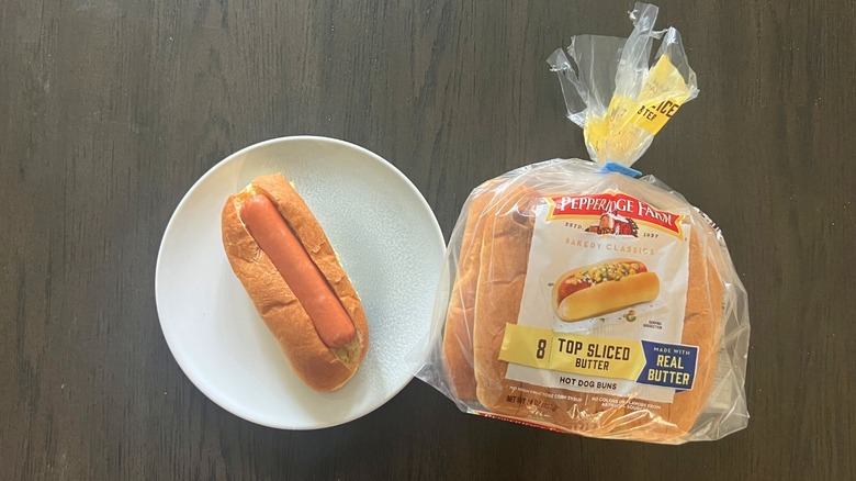 A packet of Pepperidge Farm Top-Sliced Butter Hot Dog Bun with one prepped hot dog on a white plate