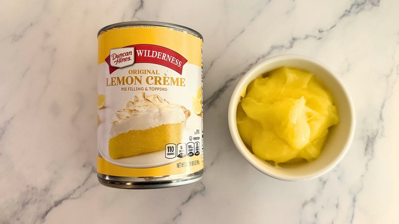 Duncan Hines lemon pie filling in white cup next to packaging on marble surface