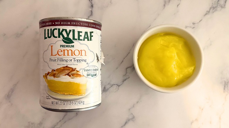 Lucky Leaf lemon pie filling in white cup next to packaging on marble surface