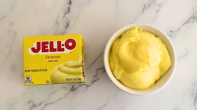 Jell-O lemon pie filling in white cup next to packaging on marble surface