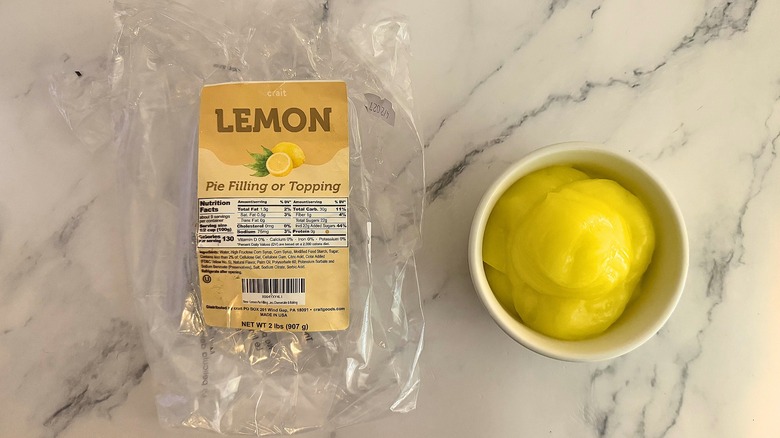 Crait lemon pie filling in white cup next to packaging on marble surface