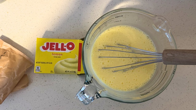 Empty Jell-O lemon pie filling box next to measuring cup with Jell-O mixture and whisk