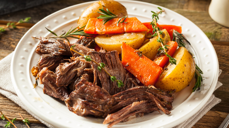 Pot roast and vegetables are served on a white plate on a set table.