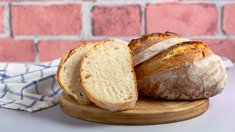 Around loaf of sourdough bread with two slices leaning on it, sitting on top of wooden cutting board