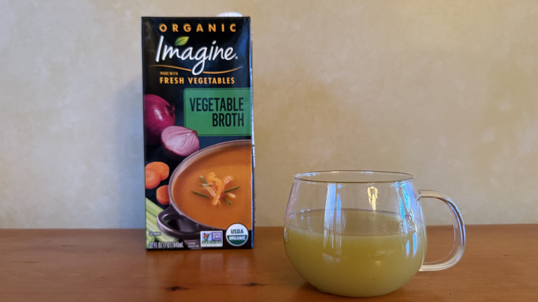 Carton of Imagine vegetable broth on wooden table with glass of broth