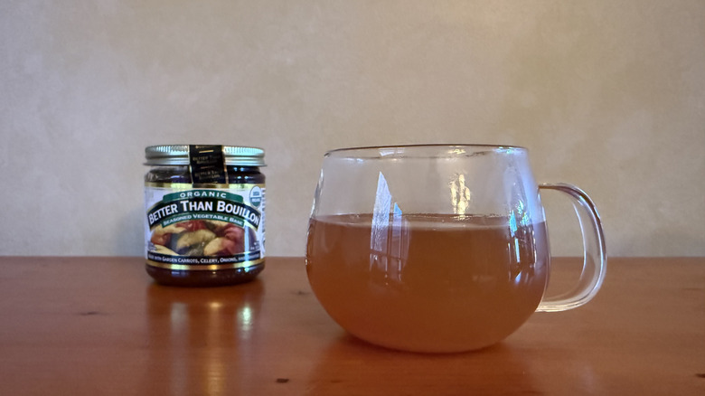 Glass jar of Better than Bouillon vegetable broth on wooden table with glass of broth