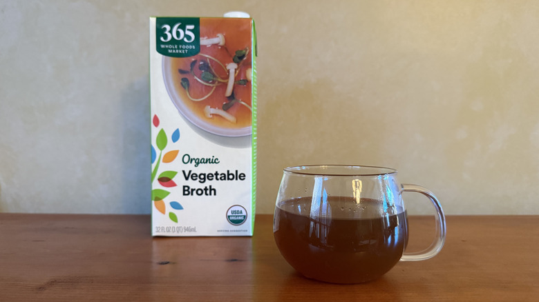 Carton of 365 vegetable broth on wooden table with glass of broth