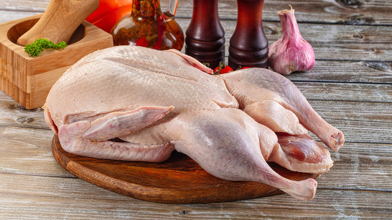 Raw whole duck on wooden board in front of seasonings