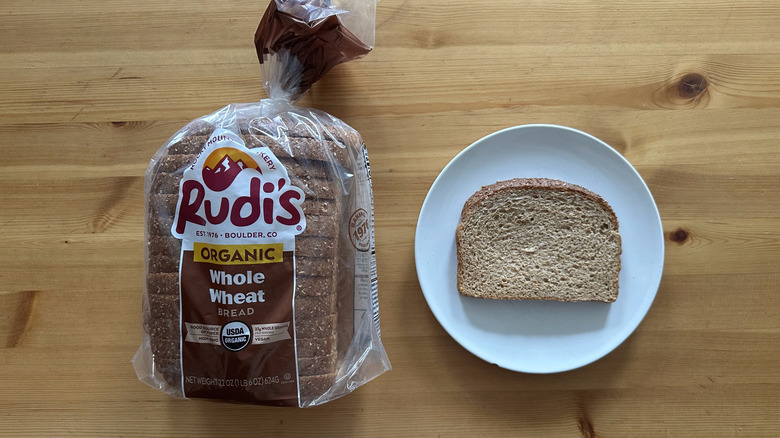 Rudi's Organic Whole Wheat Bread package and slice on a white plate on a table