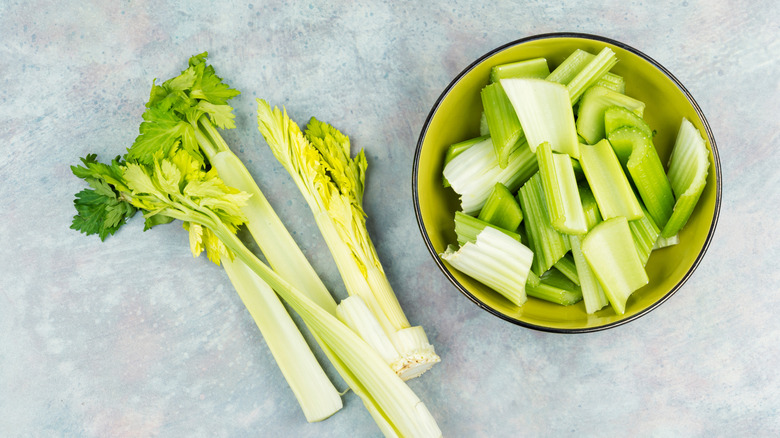 Chopped celery in a bowl with whole stalks on the table beside it.